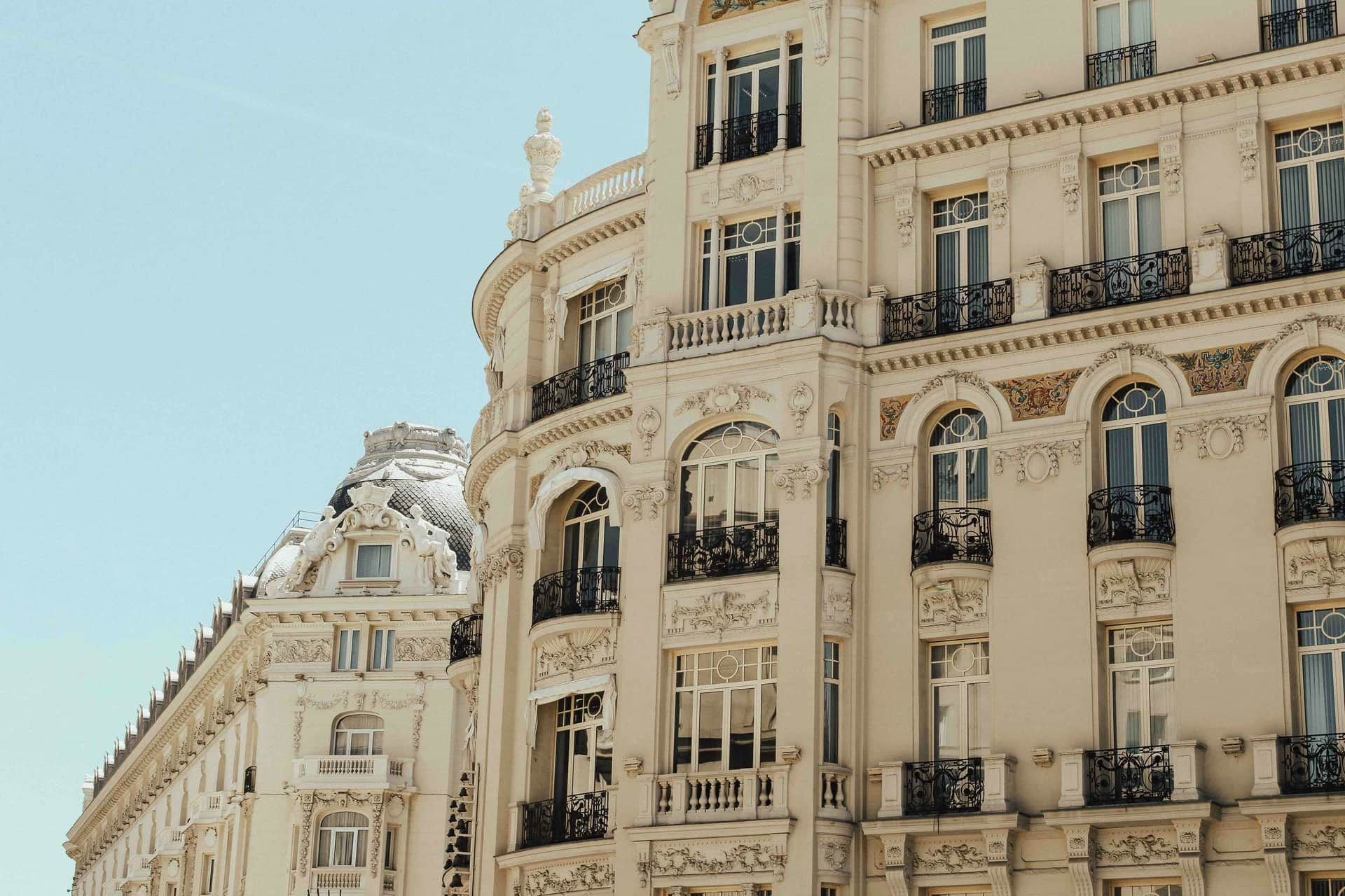 Facade of an elegant historic building in Madrid, ornate cream stone with wrought-iron balconies against a clear blue sky